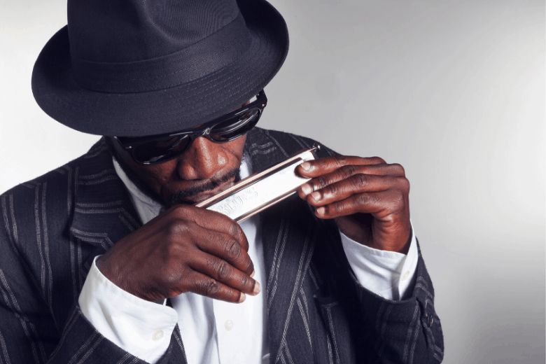 Black man with hat and shades playing the harmonica