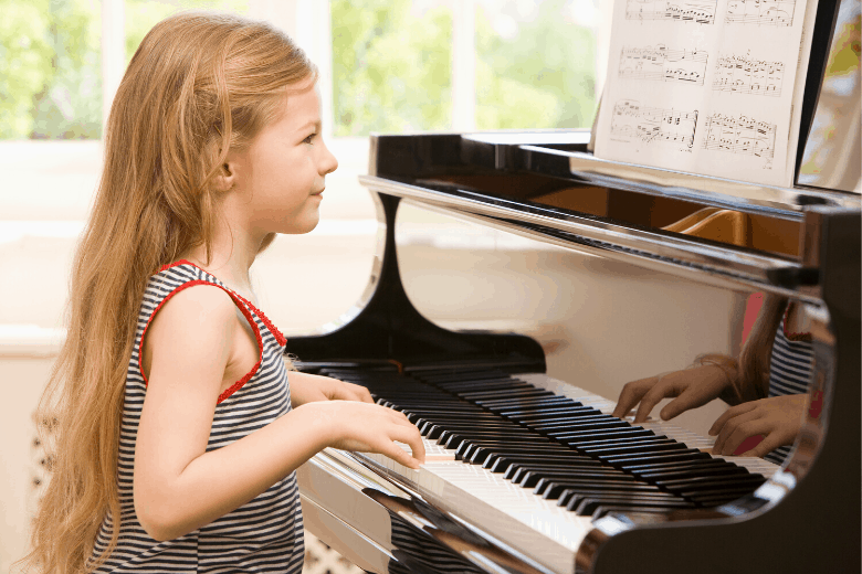 Young girl with long hair playing an upright piano and reading sheet music